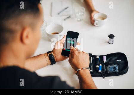 Businessman using mobile phone while doing blood sugar test at table during coffee break Stock Photo