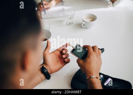 Businessman checking blood sugar level with glaucometer at table Stock Photo