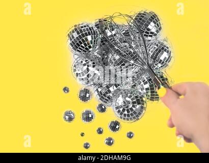 Gray silver Disco balls for decoration party shattering into small balls with whisk in hand on illuminating yellow background. Christmas New year Concept of Color of the Year 2021.  Stock Photo