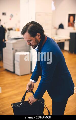 Businessman carrying bag while standing in office Stock Photo
