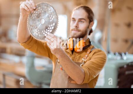A carpenter works on a woodworking machine, holding cutter at the workshop Stock Photo