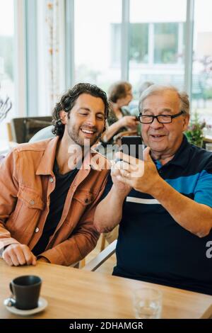 Senior man taking selfie with grandson while sitting at dining table in elderly nursing home Stock Photo