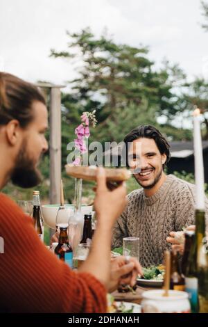 Portrait of smiling man sitting with friends at dining table in garden party Stock Photo