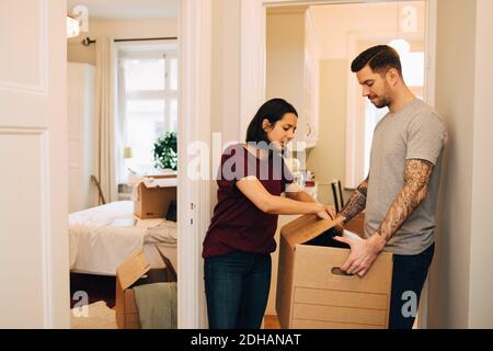 Woman unpacking box held by man in corridor at new home Stock Photo