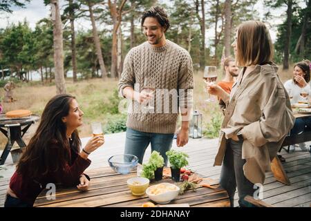 Smiling friends enjoying drinks while talking during garden party in yard Stock Photo