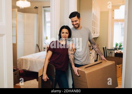 Portrait of woman standing with smiling man carrying box at home Stock Photo