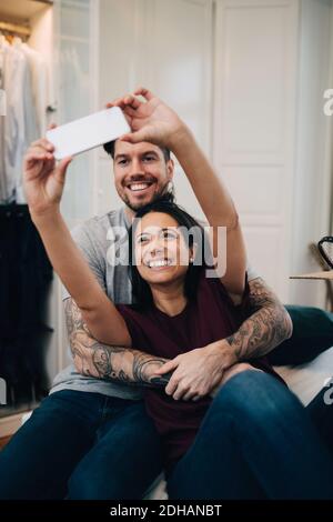 Smiling couple taking selfie on mobile phone while resting on bed in bedroom Stock Photo