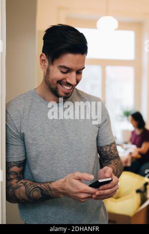 Smiling man using mobile phone while leaning on doorway at new home Stock Photo