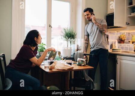 Woman looking at man talking on mobile phone in kitchen Stock Photo