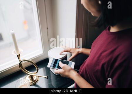 Midsection of woman using smart phone while standing by window Stock Photo