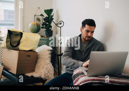 Man using laptop while sitting by boxes at home Stock Photo
