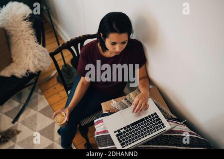 High angle view of woman having tea while using laptop by wall Stock Photo