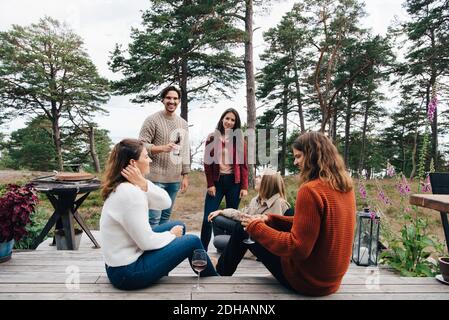 Male and female friends talking while having drinks in yard Stock Photo