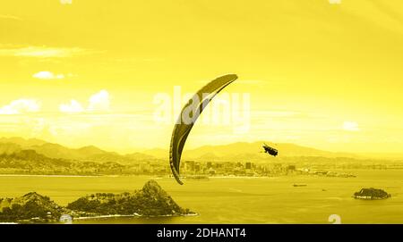 A parachute with skydiver on sunny sky background. Concept of Color of the Year 2021 with bright illuminating yellow and gray colours. Active lifestyle. Extreme sport. Aerial view of Rio de Janeiro. Stock Photo