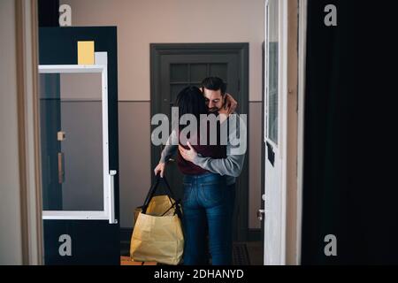 Woman embracing man with bag while standing in corridor seen from doorway Stock Photo