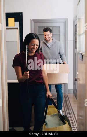 Smiling couple carrying box and bag while walking in corridor at home Stock Photo