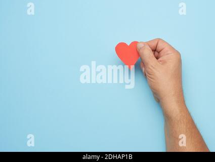 Male hand holding red paper heart on a blue background Stock Photo