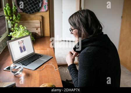Side view of businesswoman video calling female colleague on laptop in home office Stock Photo
