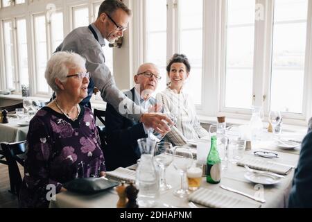 Owner serving water to senior people sitting at restaurant Stock Photo