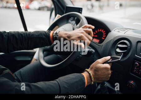 Cropped image of man holding mobile phone while driving delivery van Stock Photo