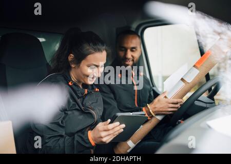 Smiling workers looking at digital tablet while sitting in delivery van Stock Photo