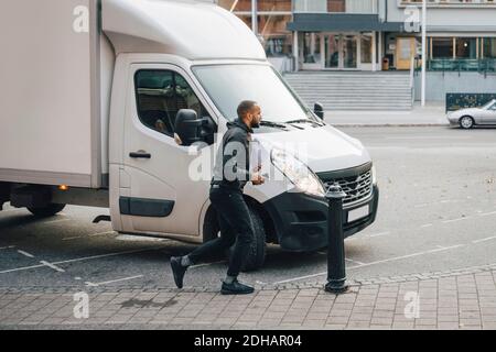 Male messenger with documents running by delivery van on street in city Stock Photo