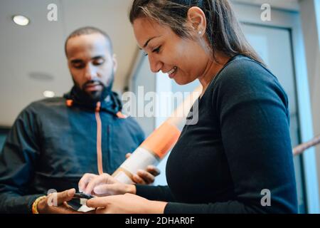 Smiling woman signing on mobile phone for her delivery from young messenger Stock Photo