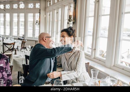 Senior man embracing woman while sitting in restaurant Stock Photo
