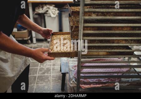 Midsection of baker keeping baked breads in tray on cooling rack at bakery Stock Photo