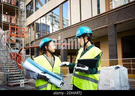 Female engineer discussing with coworker while standing at construction site Stock Photo