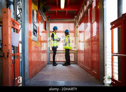 Full length of female engineers discussing while standing in freight elevator at construction site Stock Photo