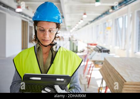 Confident female architect in reflective clothing using digital tablet at construction site Stock Photo