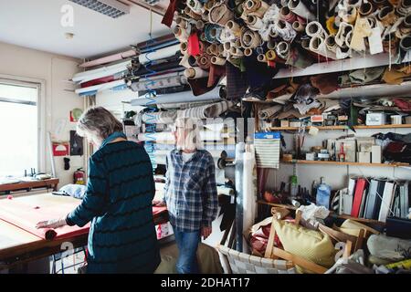 Colleagues working together while standing by shelves at workshop Stock Photo