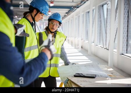Female and male engineers discussing over blueprints at construction site Stock Photo