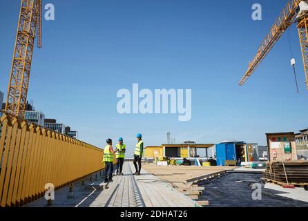 Male and female engineers discussing at construction site against blue sky Stock Photo