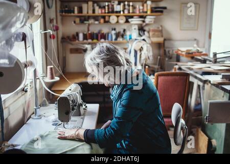 Senior female owner using sewing machine at workshop Stock Photo