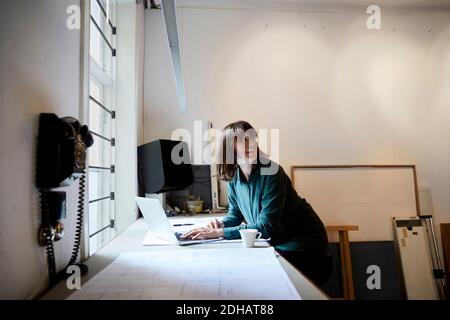 Smiling female architect looking away while using laptop in office Stock Photo
