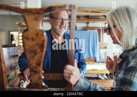 Senior owner showing wooden chair to male customer at workshop Stock Photo