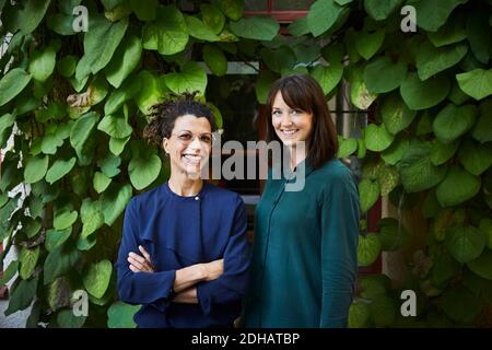 Portrait of smiling female architects standing against creeper plants in backyard Stock Photo
