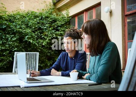 Female engineers planning over laptop at table in backyard Stock Photo