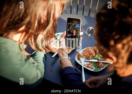 High angle view of female architect showing photograph on mobile phone to coworker at outdoor cafe Stock Photo