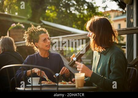 Female architects discussing while having lunch at outdoor cafe during sunny day