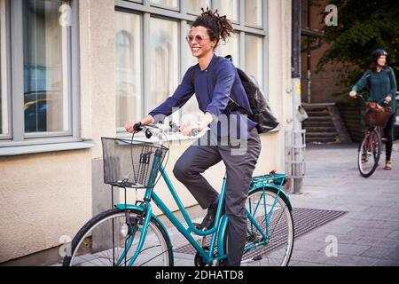 Smiling young female architect riding bicycle on street in city Stock Photo