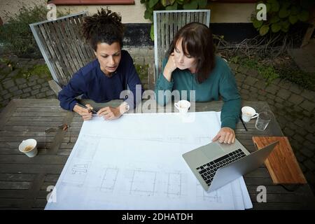 High angle view of female engineers discussing over blueprint at table in backyard Stock Photo