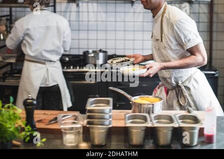 Midsection of waiter carrying food plates in kitchen at restaurant Stock Photo