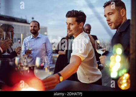 Male and female colleagues having wine while celebrating success in party after work Stock Photo