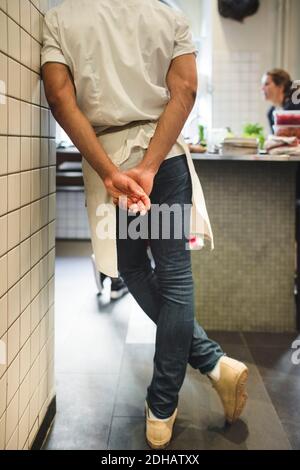 Low section of male chef standing with hands behind back in kitchen at restaurant Stock Photo