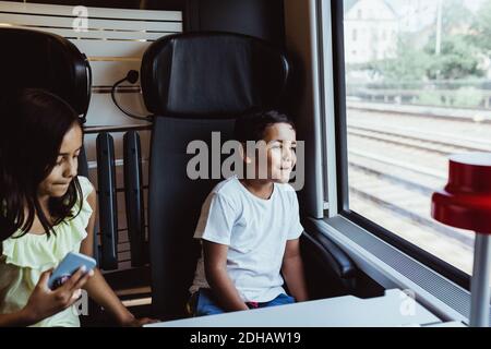 Boy looking through window while sitting with sister in train Stock Photo
