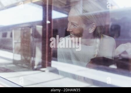 Smiling mature woman looking through window while traveling in train Stock Photo