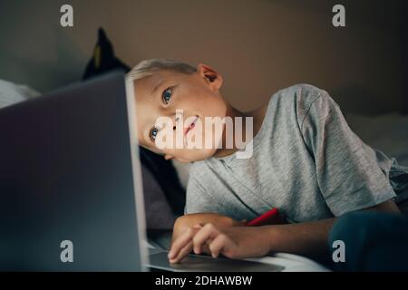 Boy using laptop reclining on bed at home Stock Photo